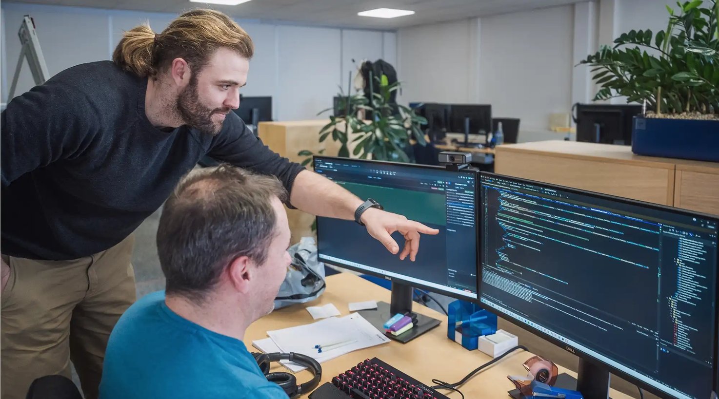 Zwei Männer blicken auf Computerbildschirme mit Softwarecode.