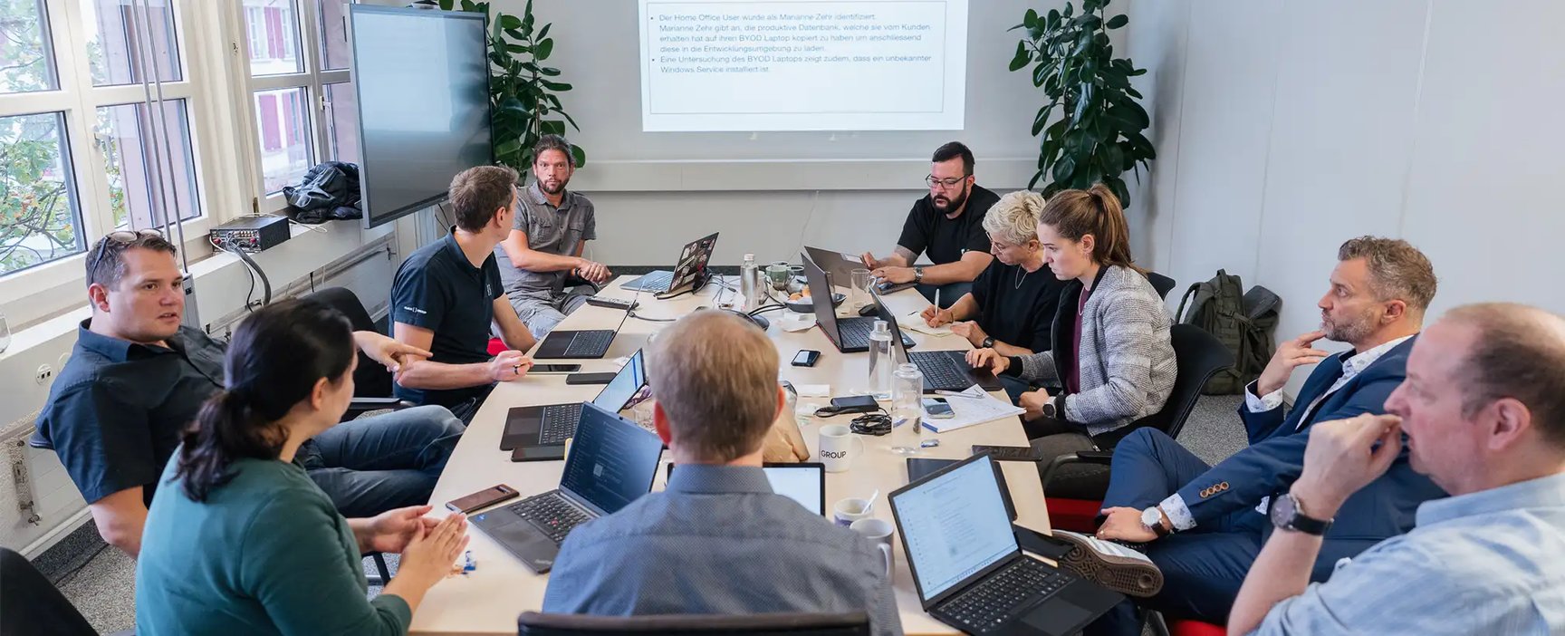 Eine Gruppe Menschen sitzen um einen Sitzungstisch herum und haben aufgeklappte Laptops