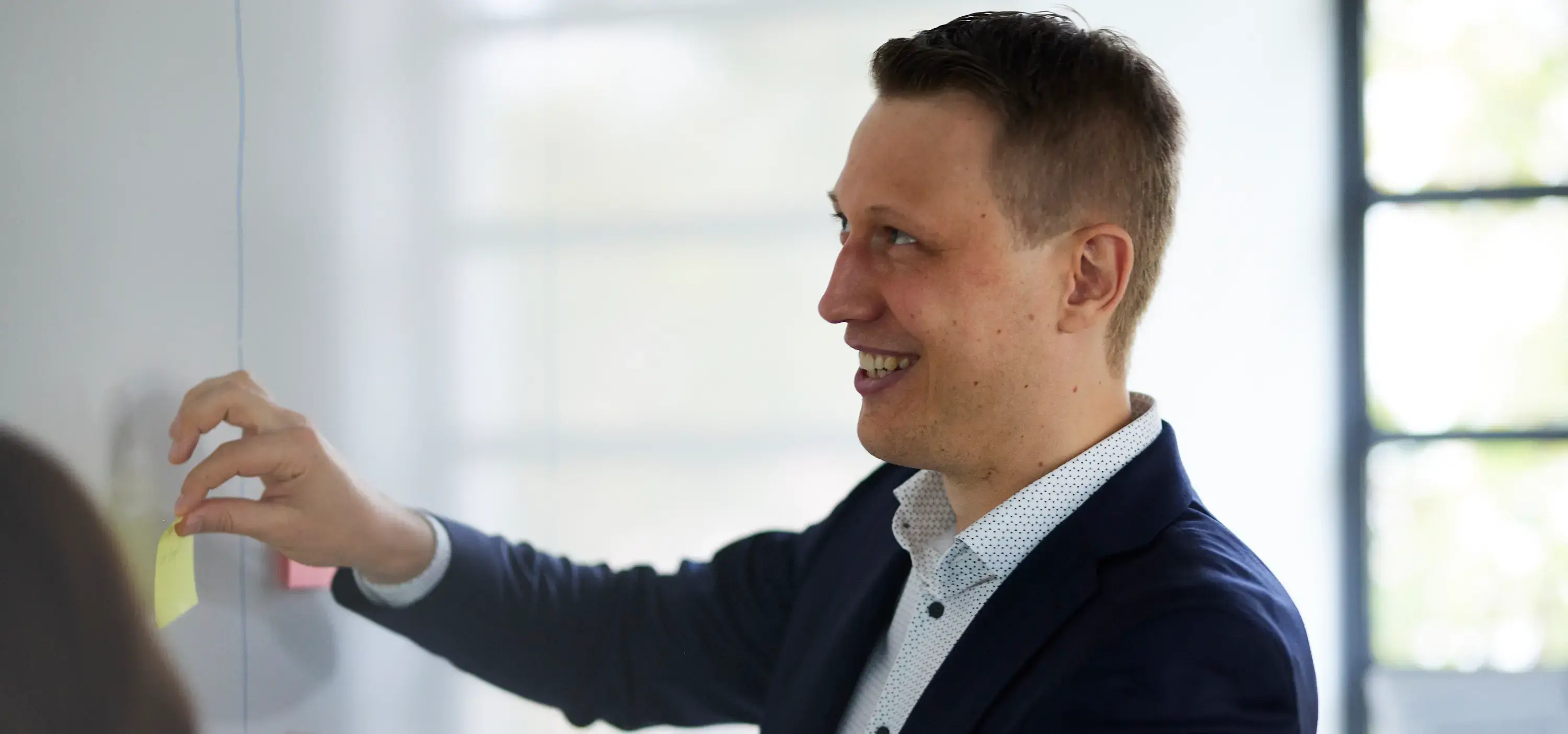 Felix Leimbach im Anzug klebt ein Post-it an ein Whiteboard